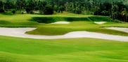 Sweeping sand bunkers separated by grassy mounds below a green at Barcelona Valley Lake Course, with woodland behind.