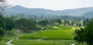 View down an undulating fairway at Barcelona Valley Lake Course towards a green, with a winding cart path and wooded hills beyond.