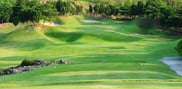 View from the 17th tee at Barcelona Valley Lake Course across rolling fairway to the green, with bunkers and a wooded hillside.
