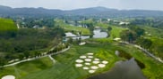 Elevated view of Barcelona Valley Lake Course showing a fairway beside water, clustered round sand bunkers and distant hills.