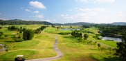 Elevated view across fairways and lakes at Barcelona Valley Mountain Course, with winding cart paths, a golf cart and wooded hills.