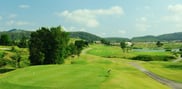 Marked teeing ground overlooking a striped fairway at Barcelona Valley Mountain Course, with a cart path, water and wooded hills beyond.