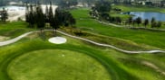 Elevated view of a foreground green and flag at Barcelona Valley Mountain Course, with a sand bunker, winding cart path, lakes and distant hills.