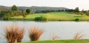 Water and reeds in the foreground of the 11th hole at Barcelona Valley Mountain Course, with a fairway, sand bunkers, trees and wooded hills beyond.