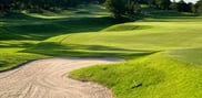 Close view of a curved sand bunker below a green, with rolling fairway in the background.