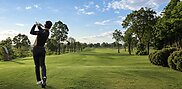 Golfer finishing a tee shot toward a tree-lined fairway with distant bunkers at Pattaya Country Club.